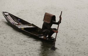 A worker on a small wooden boat pushes a paddle into the water