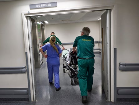 Ambulance and medical staff transport a patient in on a bed.
