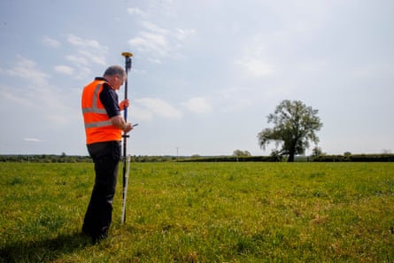 Man in orange hi-vis jacket in field with pole