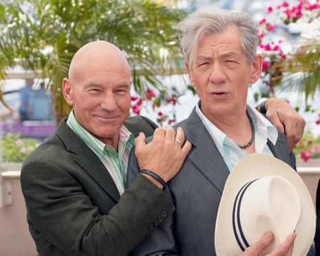 Patrick Stewart and Ian McKellen pose closely together at a film photocall, one holding a straw hat