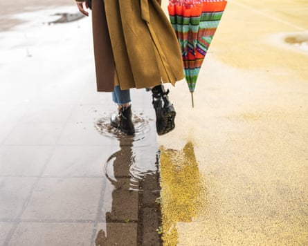 Rear view of unrecognisable woman in coat walking through puddle on rainy day at city