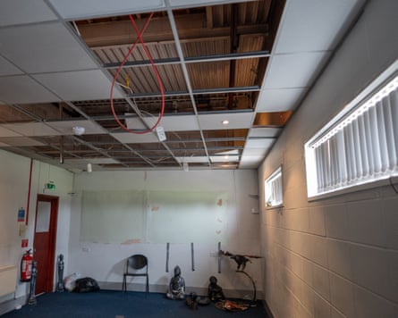 A room with missing ceiling tiles and exposed wires and plaster peeling off the walls
