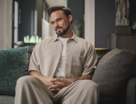A man wearing a taupe shirt and trousers and a white T-shirt.