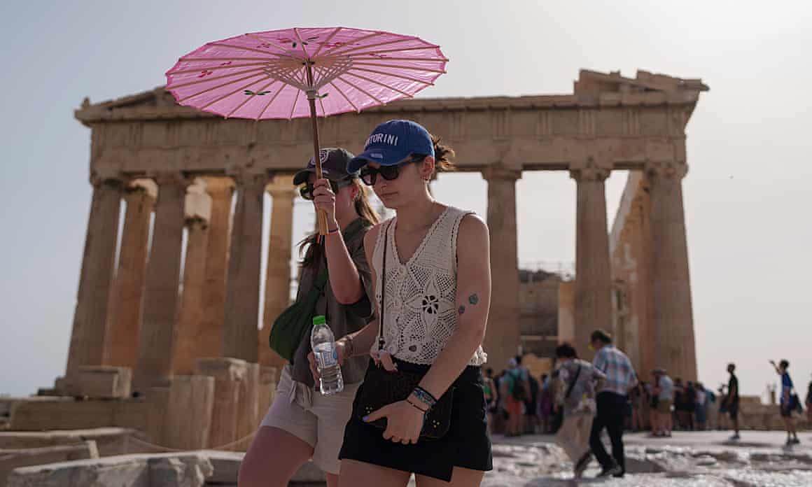 Tourists with an umbrella walk in front of the Parthenon at the ancient Acropolis in central Athens.