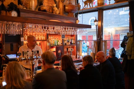 People sitting in brown bar. The bar man is bald.