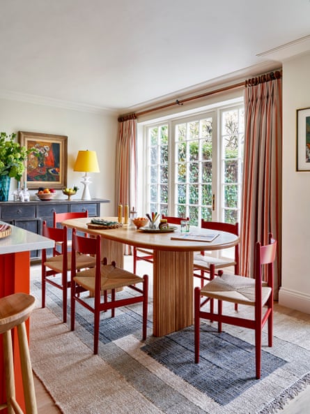 Rectangular jute rug under oval dining table next to a kitchen counter and paned curtained windows with a table lamp on a sideboard at the end