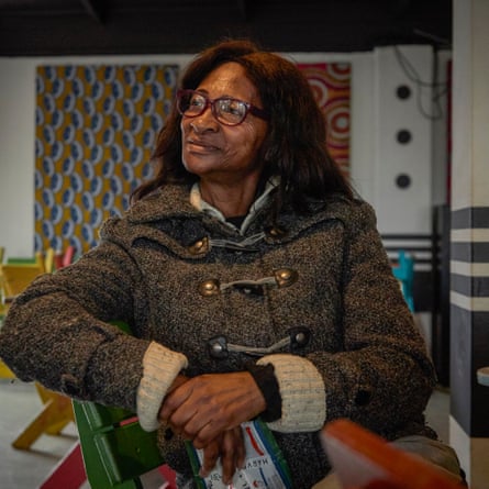 An older black women wearing glasses and a cardigan sitting in a restaurant chair.