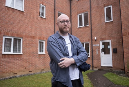 A man stands with his arms crossed in front of a block of flats