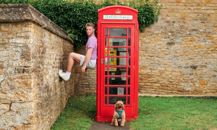 Roger Frampton with his feet against a wall and his back against a red telephone box, his dog sitting in front of the telephone box