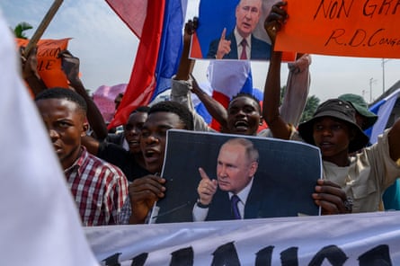 A crowd of African men at a protest hold up images of Vladimir Putin. 