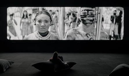 A person looks at an image of First Nations people from the Amazon in a darkened room