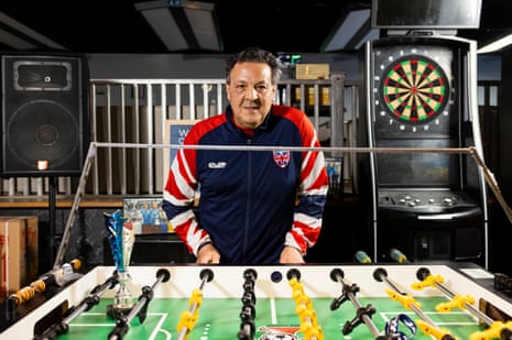 George Eid Sr wearing a red, white and blue zip-up jacket, standing behind a foosball table