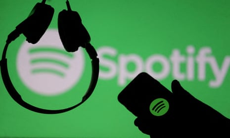 A smartphone and a headset are seen in front of a screen projection of Spotify logo