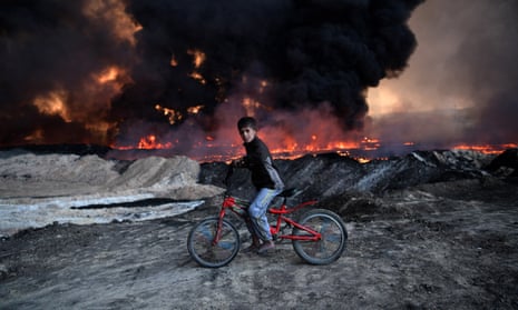 A boy passes a burning oil field