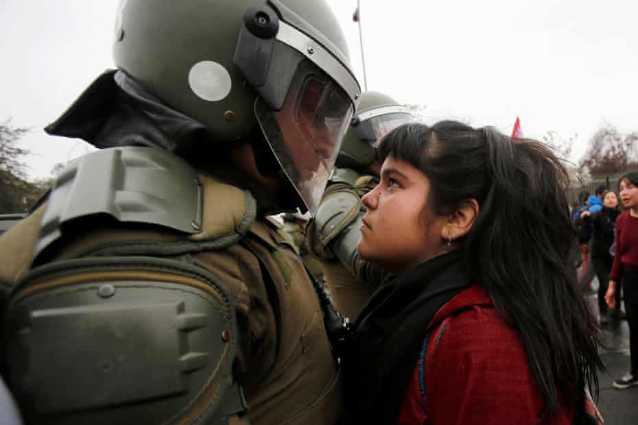 デモ参加者は、2016年9月11日、チリのサンティアゴでの1973年の軍事クーデターを記念する抗議行動中に暴動の警官を見ています。