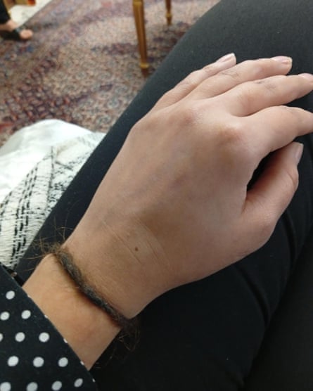 A woman's hand rests on her thigh, while round her wrist is a thin band of plaited brown hair.