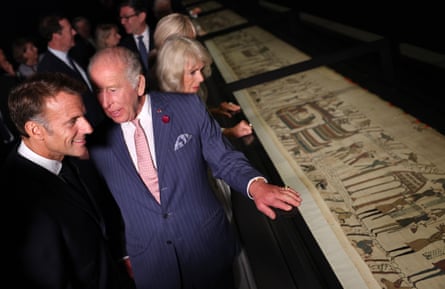 King Charles, alongside Queen Camilla, speaks to Emmanuel Macron as they view a section of the tapestry