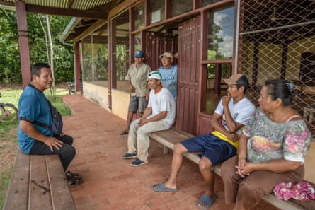 Lucio Ayala sits on a bench as he speaks with five people sitting and standing by the doorway of a building