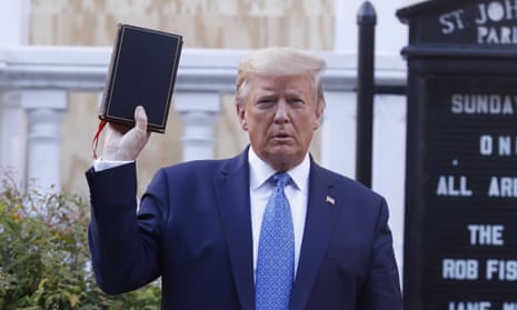 Older white man, poofy hair, blue suit, standing in front of church sign and holding up black bible in his right hand.