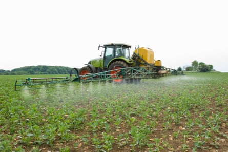 A green tractor in a Gloucestershire field spraying a crop.