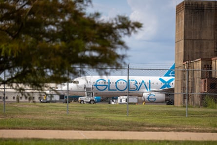 A plane sits on the tarmac behind a chain-link fence.