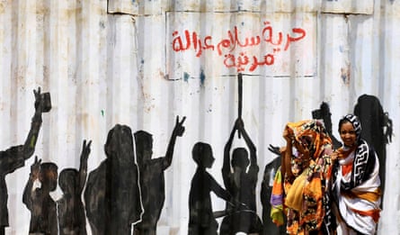 Women walk past a hoarding with graffiti of silhouetted protesters