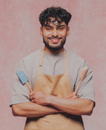 A young man with dark hair holds kitchen utensils in each hands are he crosses his arms.