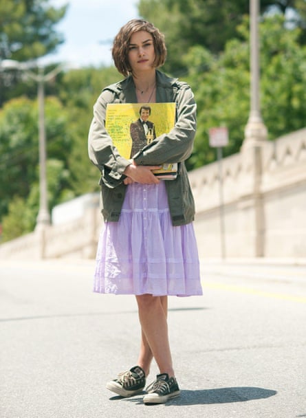 Knightley standing, wearing a mauve dress and green jacket and holding an LP.