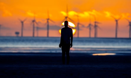 The sun sets behind Burbo Bank wind farm and Another Place at Crosby beach, Merseyside.