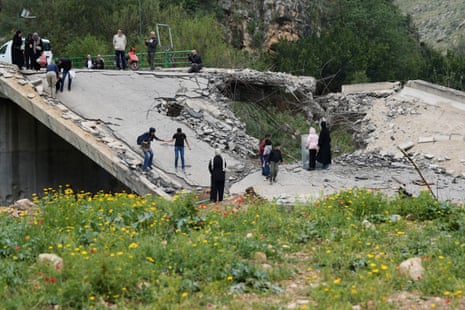 A group of people carefully traverse a broken bridge.