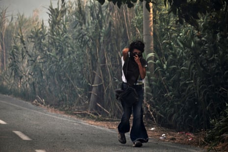 A woman walks along a road covering her face to protect herself from smoke.