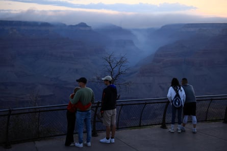 smoke in the distance of the Grand Canyon as people stand at a lookout point