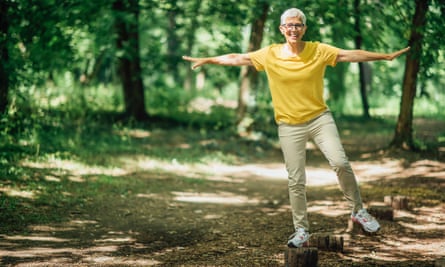 A woman balancing on one leg in woodland.