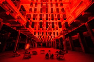 People sit in deckchairs in a turbine hall bathed in red light