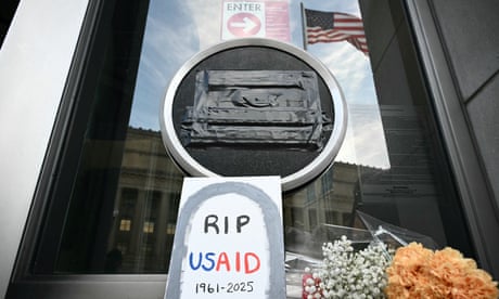 Blumen neben einem selbstgemachten Schild mit der Aufschrift „RIP USAid, 1961-2025“ vor der Tür des USAid-Gebäudes