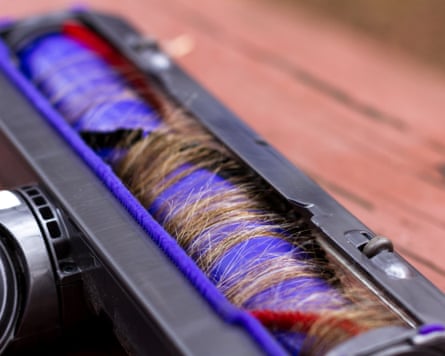 A close up of the under side of a vacuum cleaner with hair wrapped around the brushes.