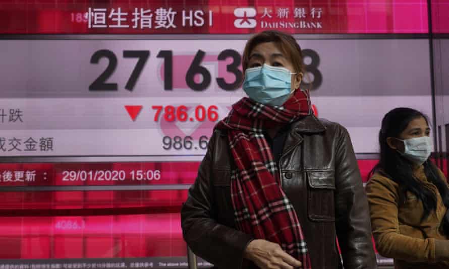 Women wearing face masks walk past a bank’s electronic board showing the Hong Kong share index.