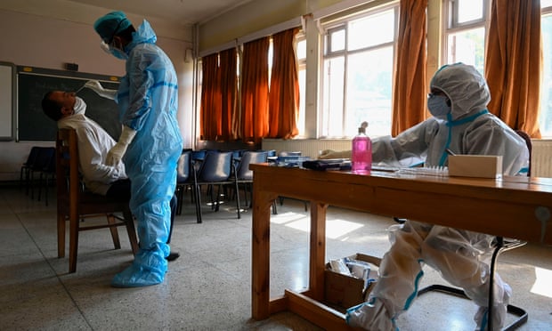 A medical worker collects a swab sample from a staff member inside a classroom for in Srinagar, India. 