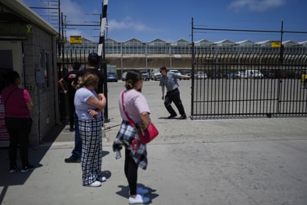 people wait outside of a warehouse as a security guard closes the gate