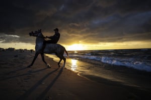Gaza City, Gaza Strip. A Palestinian youth rides his horse on the beach at sunset
