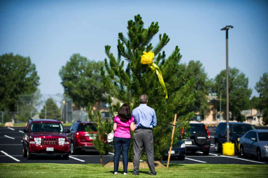 Caren Teves and Tom Teves stand in front of a tree with a ribbon bearing the name of their late son, Alex Teves.