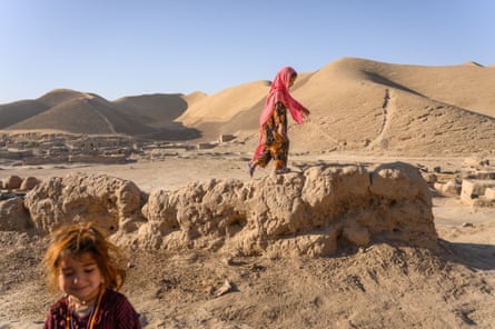 Two girls play in a sandy rural landscape.