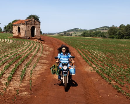 A man in drag rides a motorbike through a field