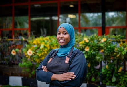 A young Somali woman standing in front of a shrub with yellow flowers