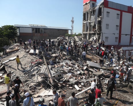 A crowd of people milling over large pile of rubble