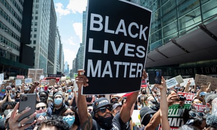 A protester in Times Square holds up a large sign that reads ‘Black Lives Matter’ with thousands of people behind him.