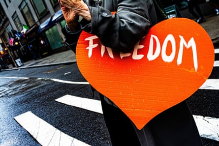 A heart-shaped sign reading ‘Freedom’ tucked under the arm of a person walking.