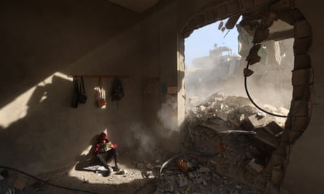 A Palestinian boy reading in the sunlight streaming through the destroyed wall of a house