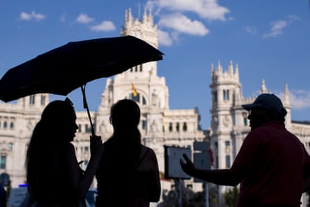 Tourists shielding themselves from the sun with an umbrella by the Cibeles Palace in the centre of Madrid.