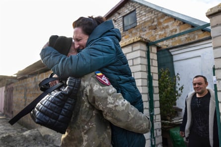 Ukrainian soldier Nikolai Skelsarov hugs his mother, Elena Skelsarova, watched by brother-in-law Kobilsky Taras. The soldier was returning home from eight months on the battlefield on 15 November after Ukrainian forces reclaimed Kherson